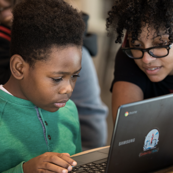 A parent watching their child work on a laptop