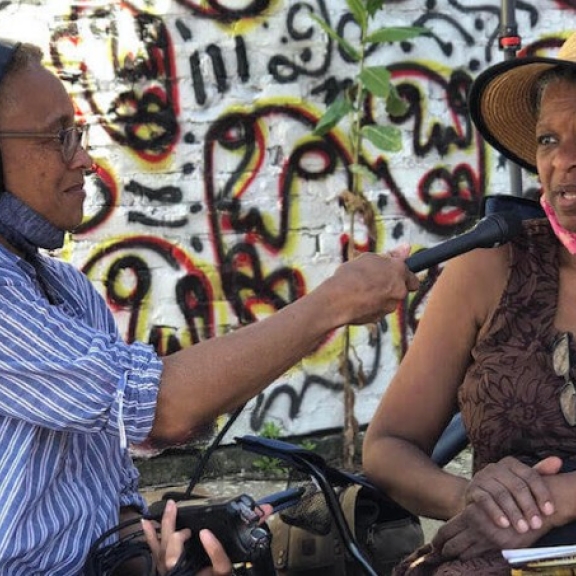 A person wearing headphones holds up a microphone for the person sitting next to them to speak into