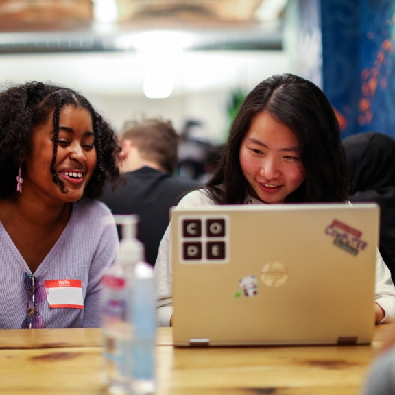 Two people seated at a table smiling at a laptop