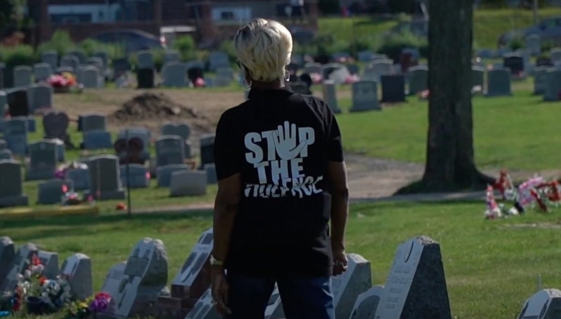 A person wearing a Stop The Violence black t-shirt looks at the graves in a cemetary