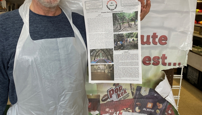 A person wearing a gray shirt, gray knit hat and a plastic apron holds up a newspaper