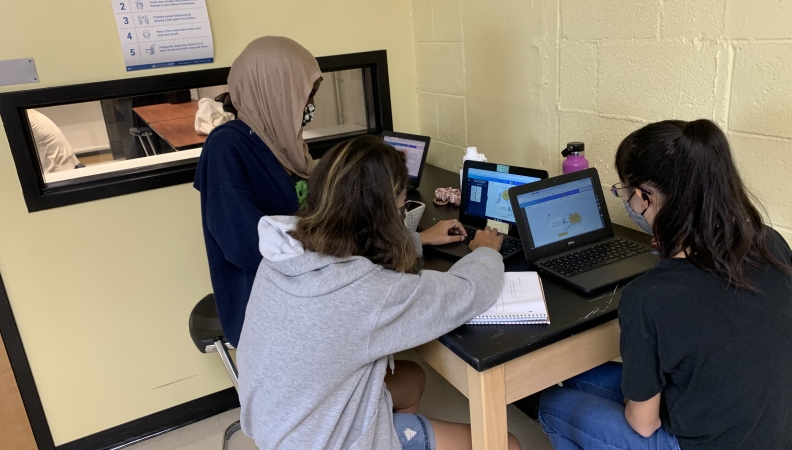 Three teenagers work on laptops at a desk