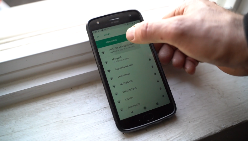 A hand using an android phone on a windowsill to connect to wifi