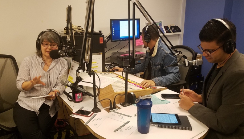 three people talking on microphones during the recording of a radio show