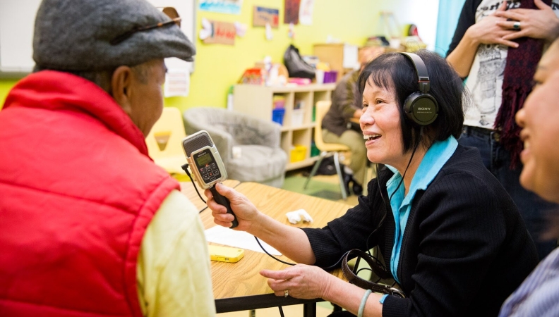 a woman holding a microphone to interview a person wearing a red vest