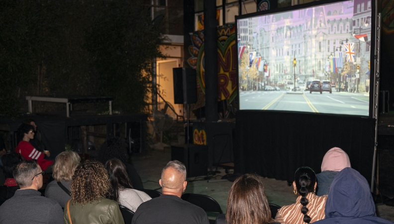 a group of people seated outdoors watching a movie screen 