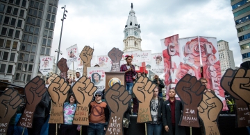 a rally in front of Philly's city hall with a group of people holding cut out signs of fists
