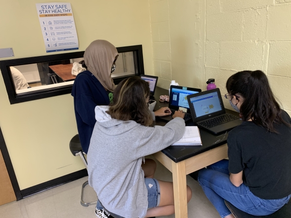 Three teenagers work on laptops at a desk