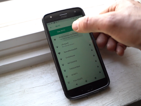 A hand using an android phone on a windowsill to connect to wifi