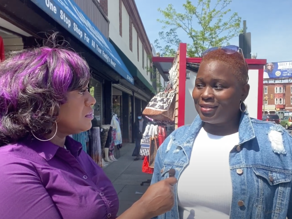 a woman with purple hair highlights and wearing a purple top interviews another woman wearing a jean jacket and a low cut fade hairstyle