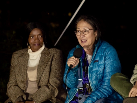 a woman speaks into microphone during a film panel conversation with another woman looking at her and listening intently