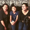 Three people, one of them a young person, sit on a cozy black sofa, smiling at the camera