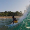 A person in yellow trunks surfing on a blue board with an island in the background