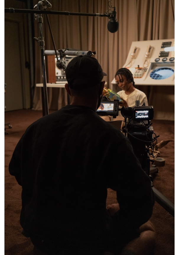 A film crew member looks through a viewfinder as an actor looks at something in their hands