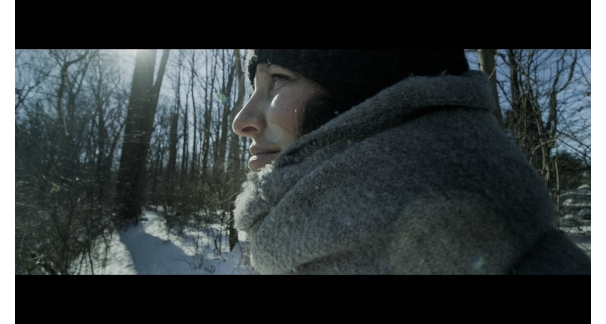 Profile of a person standing outside on a snowy day wearing a scarf and hat