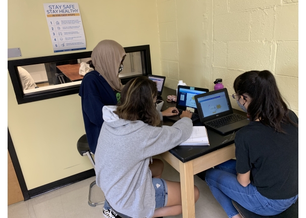 Three teenagers work on laptops at a desk