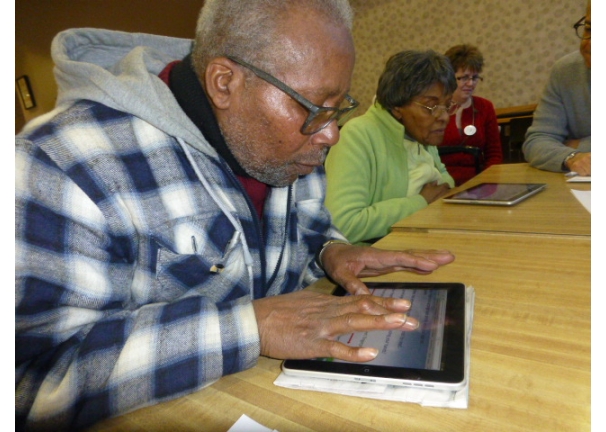 A group of older people seated at a table using tablets