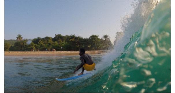 A person in yellow trunks surfing on a blue board with an island in the background
