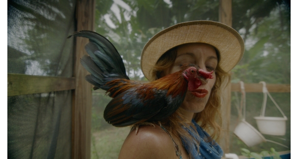 A person purses their lips towards a rooster perching on their shoulder