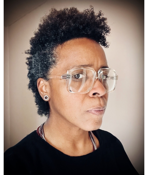 Profile view of a Black person with graying natural hair wearing glasses