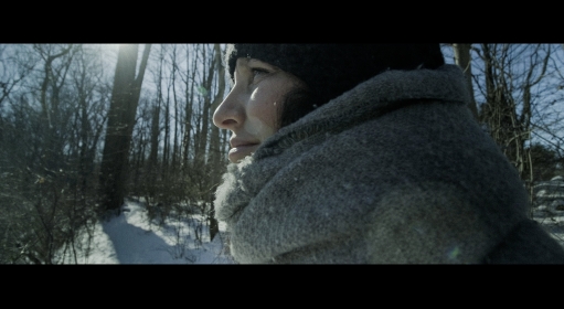 Profile of a person standing outside on a snowy day wearing a scarf and hat
