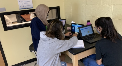 Three teenagers work on laptops at a desk