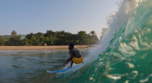 A person in yellow trunks surfing on a blue board with an island in the background