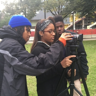 Three people adjusting a video camera in a park