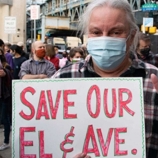 a man standing at a demonstration holding a sign saying "Save Our El & Ave" and flashing a peace sign
